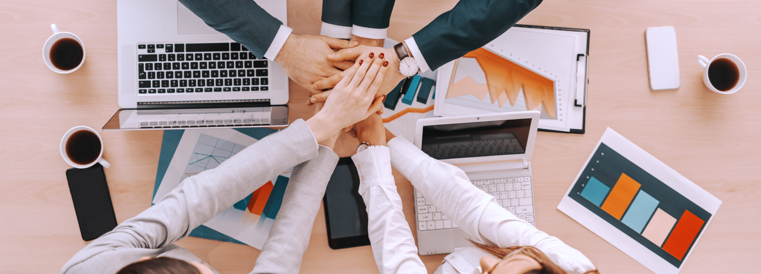 Top view of businesspeople stacking hands above table. On table laptops and charts. Good habits are formed; bad habits we fall into. About Desuvit